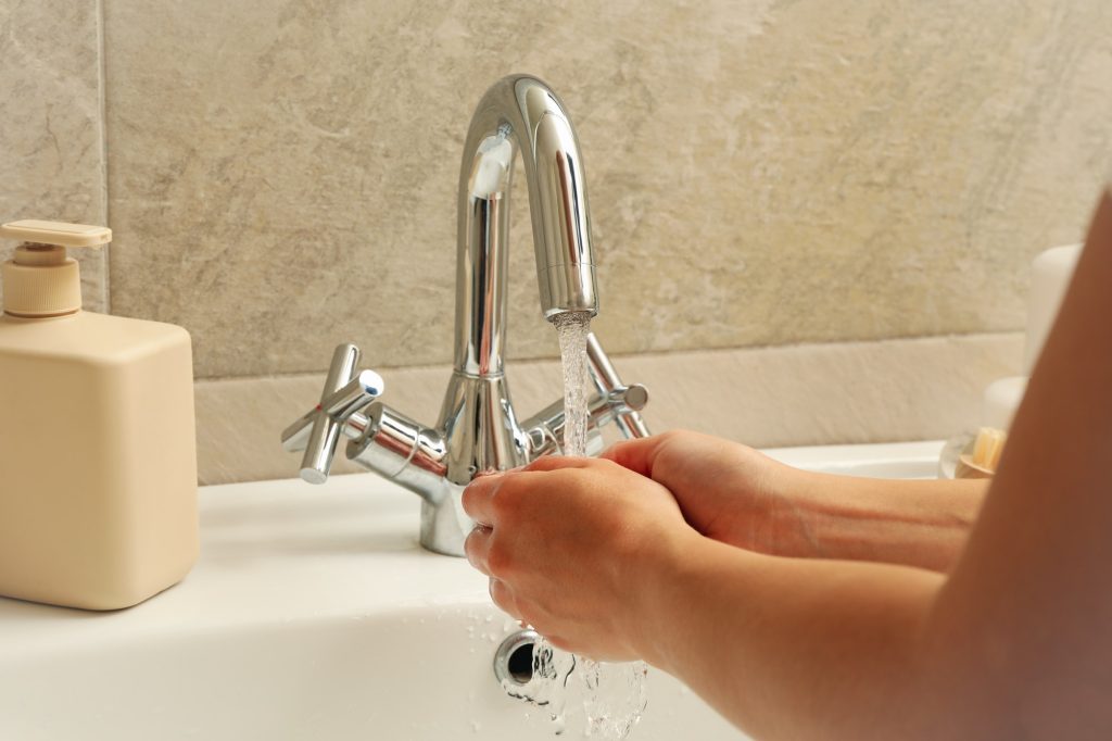 Woman washing hands under the water tap in sink